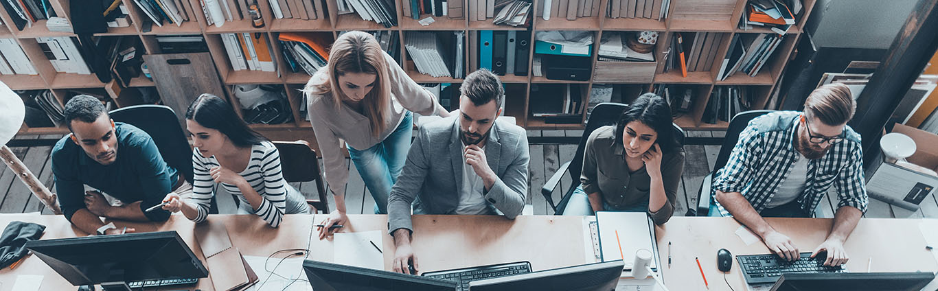 Mensen zitten naast elkaar achter een bureau te werken met computers