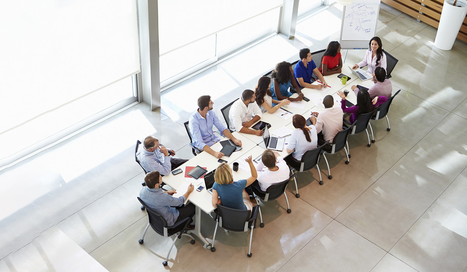 Mensen zitten aan een lange tafel met tablets en laptops