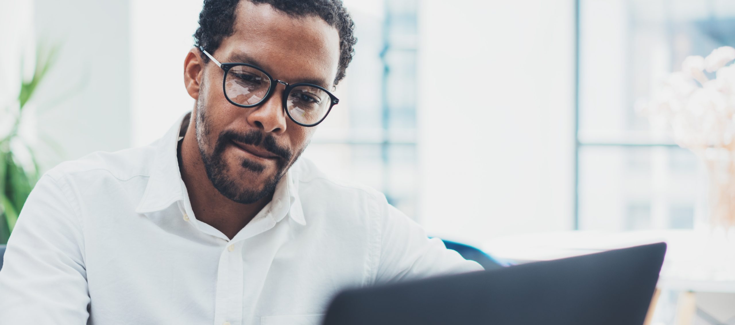 Black corporate man wearing glasses looking at laptop screen
