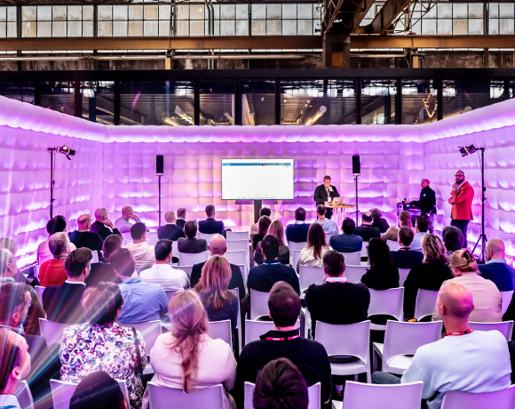 Foto van een zaal met een presenatie en publiek