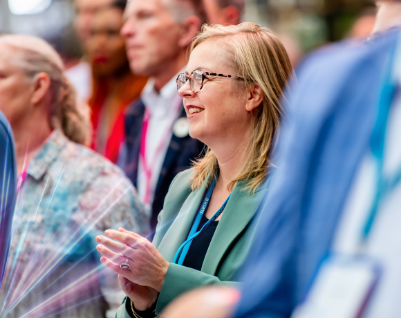 Foto van publiek, ingezoomd op een vrouw die glimlacht en in haar handen klapt