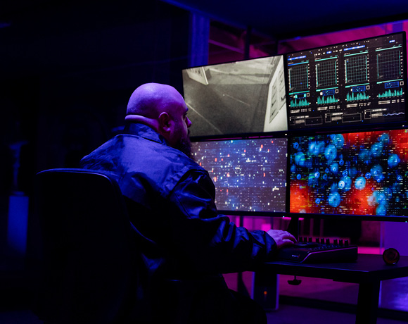 Bewaker zit in een donkere ruimte en houdt nauwkeurig camerabeelden en cyberaanvallen in de gaten