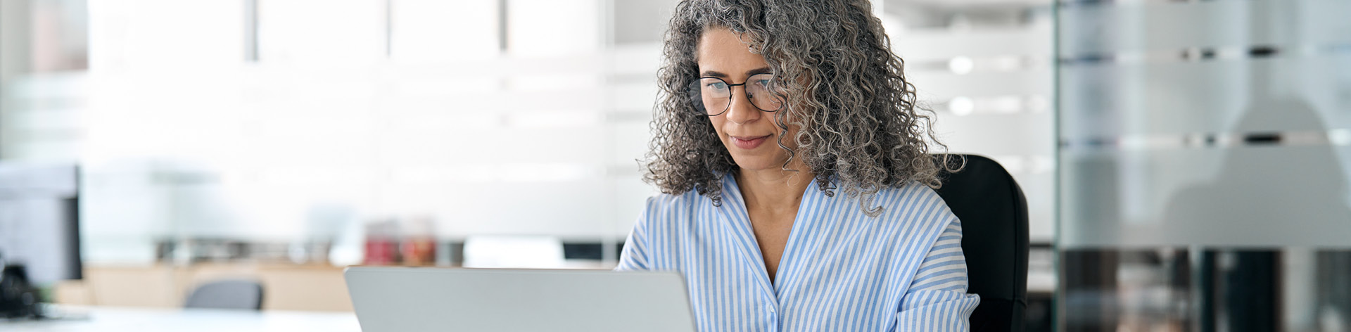 Witte vrouw met grijs krullend haar op kantoor, zit achter een laptop