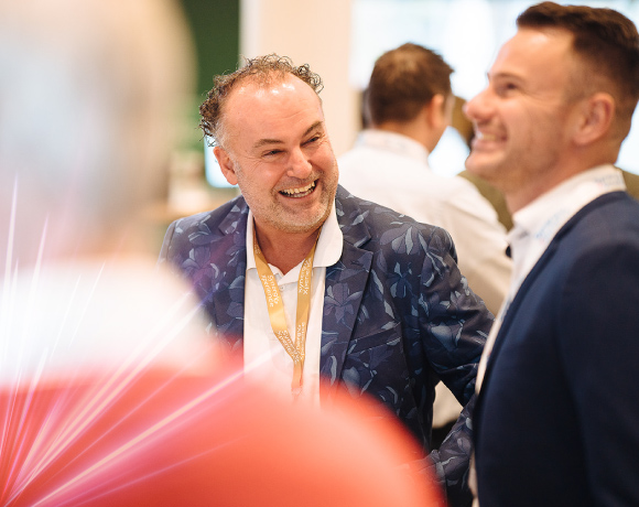 Foto van een man in gesprek met een andere man, met een grote glimlach