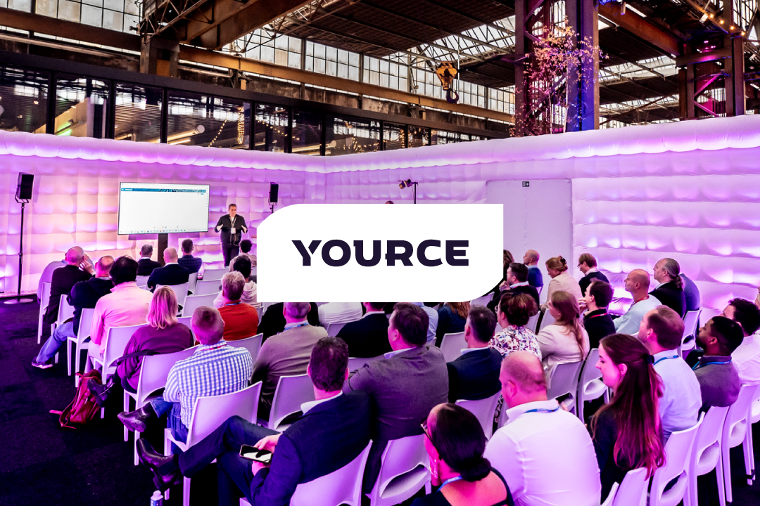 Foto van een presentatie met publiek, met daarop een logobalkje met het logo van Yource