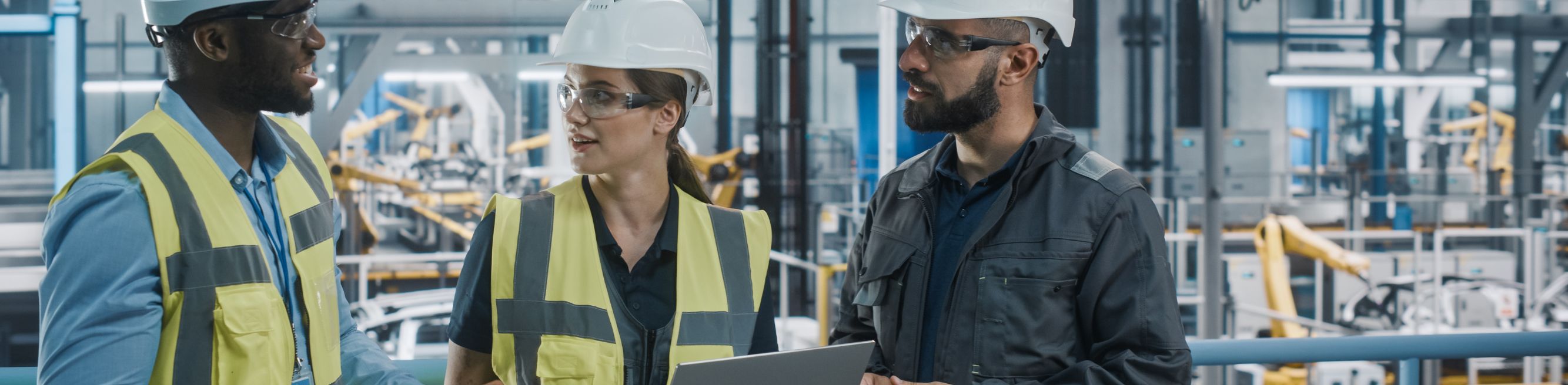 Industriële IT-professionals in veiligheidskleding werken samen in een fabriek of werkplaats. Ze bekijken gegevens op hun laptop
